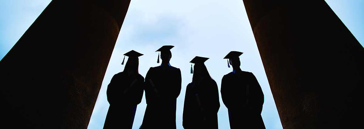 Four graduates stand between columns of a building