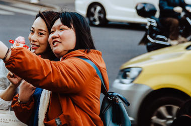 Two young people taking a photo on a smartphone with a busy street in the background