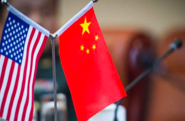 Small U.S. and China flags on a table in the foreground of a meeting