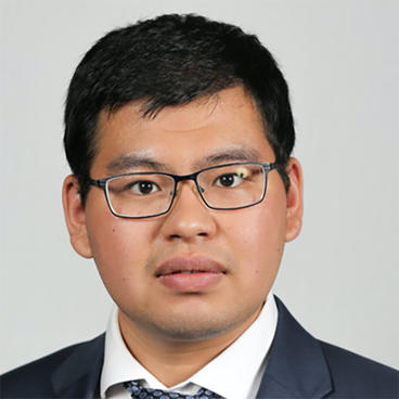 Mingfeng Shi looks at the camera wearing his hair parted to the side and glasses. He is dressed in a business suit.